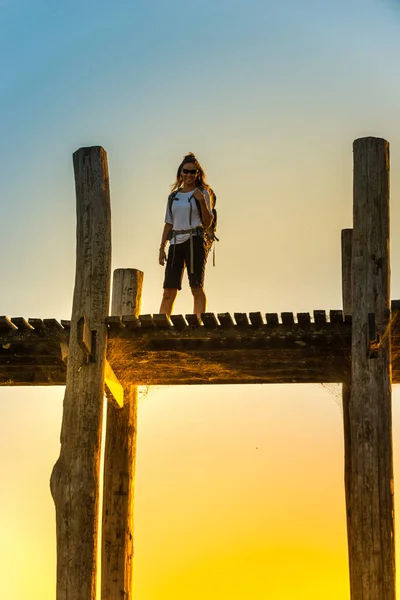 Backpacker turista de pé em madeira U Bein ponte ao pôr do sol em — Fotografia de Stock