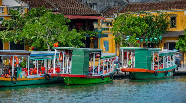 Barcos turísticos en el río Thu Bon con viejos edificios amarillos en — Foto de Stock