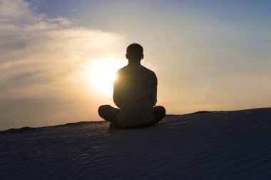 Gün batımında lotus pozisyonunda bir adam