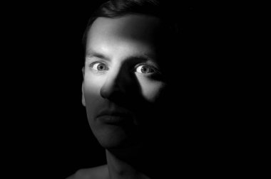 Siyah arka planda tek bir ışık kaynağı olan bir adamın siyah-beyaz dramatik portresi