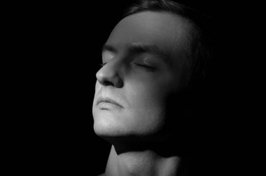 Siyah arka planda tek bir ışık kaynağı olan bir adamın siyah-beyaz dramatik portresi