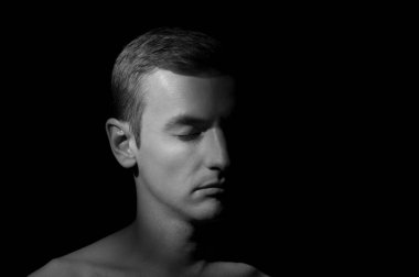 Siyah arka planda tek bir ışık kaynağı olan bir adamın siyah-beyaz dramatik portresi