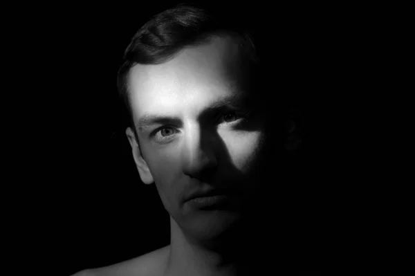 Siyah arka planda tek bir ışık kaynağı olan bir adamın siyah-beyaz dramatik portresi