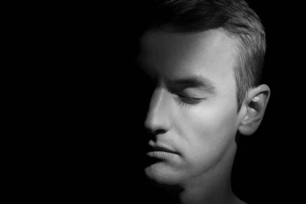 Siyah arka planda tek bir ışık kaynağı olan bir adamın siyah-beyaz dramatik portresi