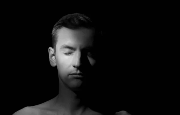 Siyah arka planda tek bir ışık kaynağı olan bir adamın siyah-beyaz dramatik portresi