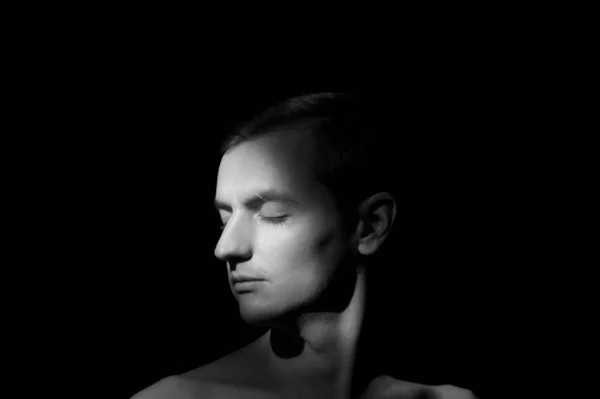 Siyah arka planda tek bir ışık kaynağı olan bir adamın siyah-beyaz dramatik portresi