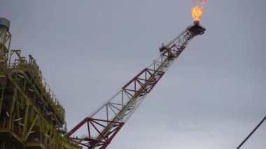 Bulutlu gökyüzü ile denizin ortasında petrol sondaj platformu platformu üzerinde yanan gaz flare düşük açılı görünüş.