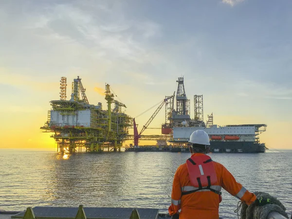 Oil and gas industry. Marine crew standing on supply vessel looking oil and gas platform during sunrise.