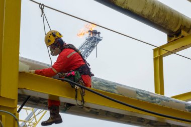 Yükseklerde çalışıyor. Kişisel Koruyucu Ekipman (PPE) takan bir abseiler örneğin solunum koruması, sert şapka, emniyet kemeri, el koruması, göz koruması ve arka plan işaret fişeği ile boyama faaliyetleri için yapının üzerinde oturan örtüler 