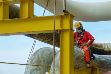 Yükseklerde çalışıyor. Kırmızı tulum giyen bir abseiler ve solunum koruması, sert şapka, emniyet kemeri, el koruması ve göz koruması gibi Kişisel Koruyucu Ekipman (PPE) boru hattına bakıyor.