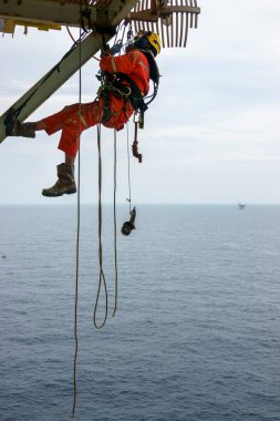Yükseklerde çalışıyor. Kırmızı örtü giyen bir grup abseiler ve sert şapka, emniyet kemeri, el koruması ve göz koruyucusu gibi kişisel koruyucu ekipmanlar iğne pulu kullanılarak aşınmanın kaldırılması için erişim platformu altında asılı durumdalar.