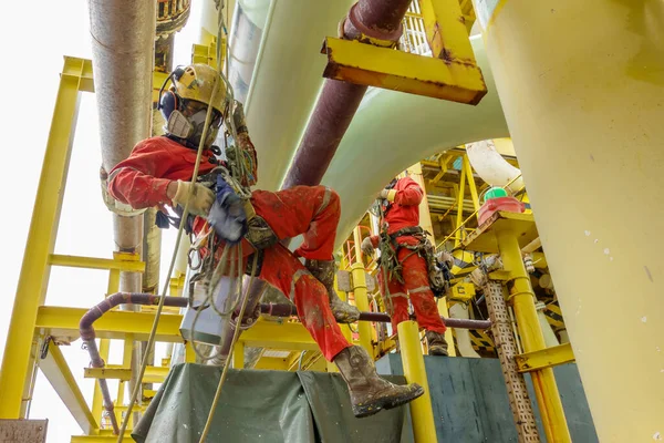 Yükseklerde çalışıyor. Solunum koruması, kasket, emniyet kemeri, el koruması, göz koruması ve boyama faaliyetleri için boru hattında asılı ve ayakta duran bir grup halat taşıyıcısı (PPE).