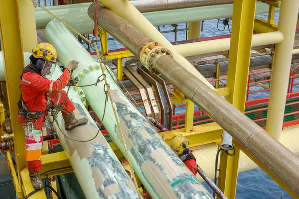 Yükseklerde çalışıyor. Bir grup abseiler kırmızı kapaklı ve kişisel koruyucu ekipman (PPE) (solunum koruması, sert şapka, emniyet kemeri, el koruması ve göz koruması) kullanılarak boyama faaliyetleri için halat erişim tekniği kullanırlar..