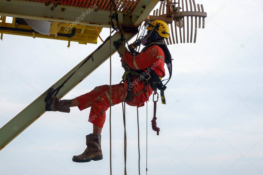 Working at height. A group of abseilers wearing red coverall and Personal Protective Equipment (PPE) such as hard hat, harness, hand protection and eye protection hanging under access way platform to check the corrosion of the structure.