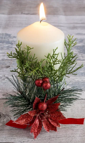 Белая горящая свеча с цветком падуба и зеленой веткой — стоковое фото