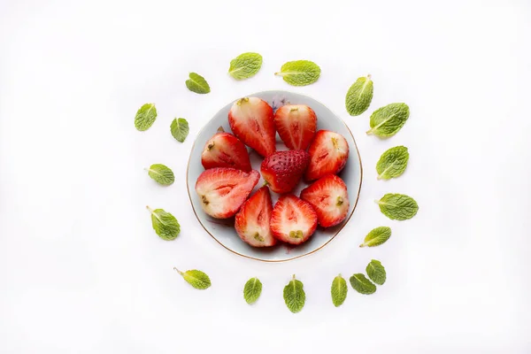 Skål med skurna jordgubbar på vit bakgrund med grönmynta blad — Stockfoto