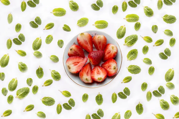 Skål med skurna jordgubbar på vit bakgrund med grönmynta blad — Stockfoto