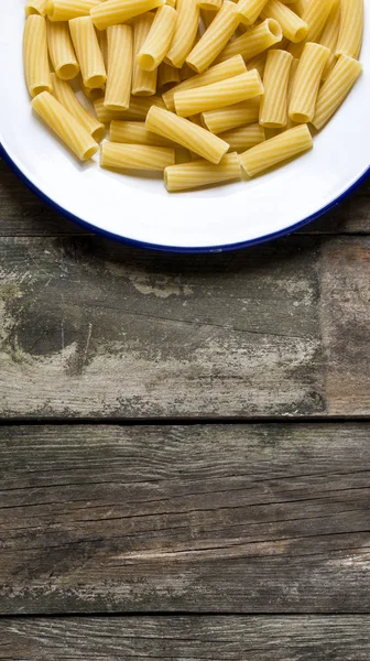 Ruwe macaroni geserveerd op een plaat op een rustieke houten tafel, — Stockfoto