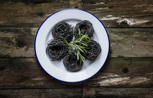 Black pasta nests on a plate on rustic wooden table, — Stock Photo, Image