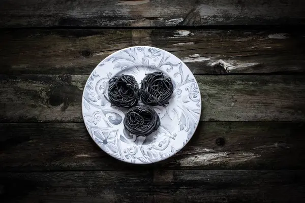 Black pasta nests on a plate on rustic wooden table, — Stock Photo, Image