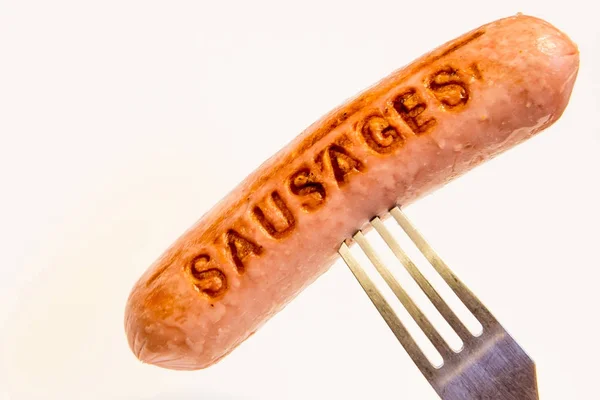 Sausage with an inscription pinned on a fork, on a white background. — Stock Photo, Image