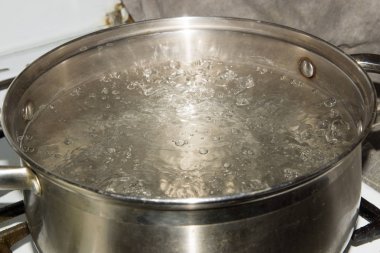 Paslanmaz çelik tencere üzerinde bir gaz sobası ve su kaynar.