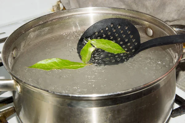 The pot of boiling water, which omit the Bay leaves, give the dish a savory aroma and taste. — Stock Photo, Image