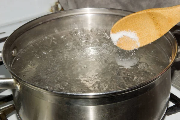 В кипящую воду лейте соль деревянной ложкой . — стоковое фото