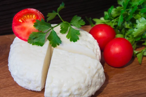 Fresh cheese with excellent taste and aroma. Cheese on wooden cutting Board with tomatoes and fresh herbs. — Stock Photo, Image