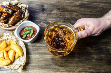 Susam ile güzel kokulu ve keskin soslu tavuk kanatları. Bir bardak taze soğuk bira ve taze domates ve otlar rustik domates soslu patates kızartması