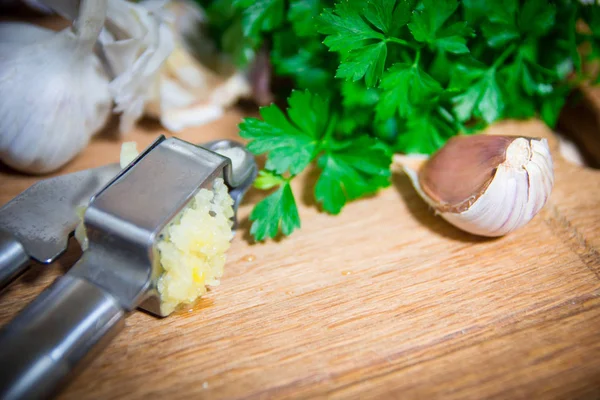 Crushing garlic to add to the dish. Whole and chopped garlic on a cutting Board made from natural oak. Fresh parsley.