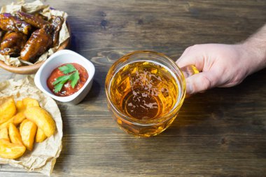 Susam ile güzel kokulu ve keskin soslu tavuk kanatları. Bir bardak taze soğuk bira ve taze domates ve otlar rustik domates soslu patates kızartması