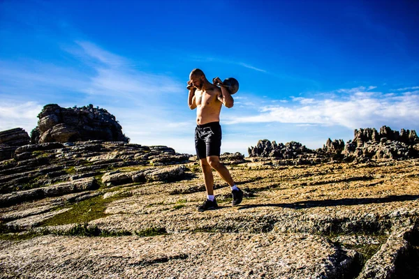 Hayır gömlek bir dağın tepesinde iki kettlebells tutan adamla