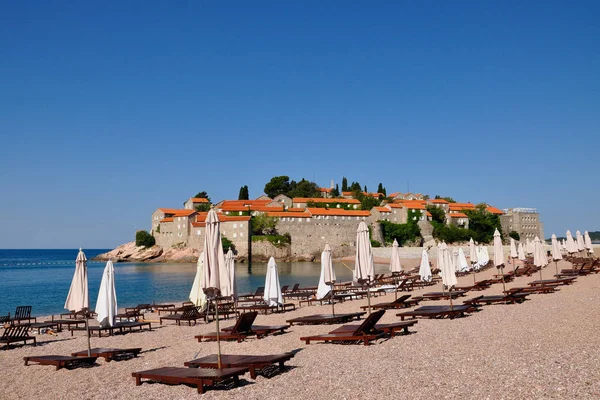 Una vista de la isla de Sveti Stefan en un día de verano con sombrillas y tumbonas, Montenegro — Foto de Stock