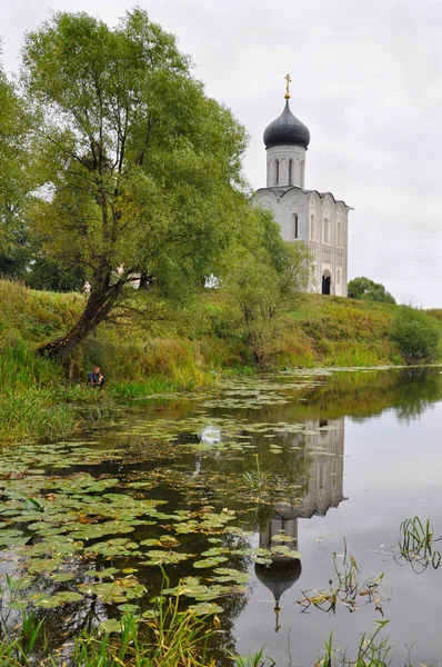 O menino está pescando para a Igreja da Intercessão sobre o Nerl com um monumento histórico da UNESCO como parte do Anel de Ouro da Rússia Fotos De Bancos De Imagens