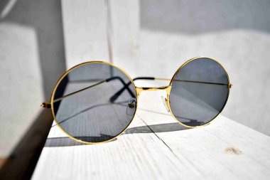 Siyah gözlüklü altın güneş gözlükleri beyaz ahşap bir sütunun arkasında yatıyor.