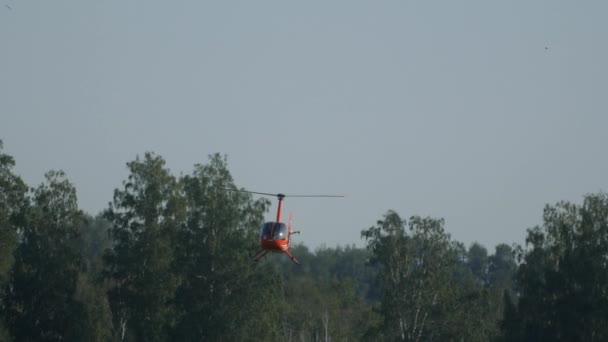 L'hélicoptère robinson orange vole au ralenti à travers la forêt et fait une boucle — Video