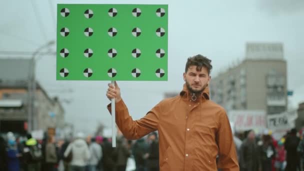 Man med en tom fana i handen vid ett politiskt möte tittar på kameran. — Stockvideo