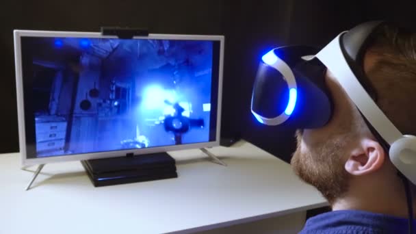 Persona se sienta en el casco de realidad virtual mira de cerca frente al monitor con el juego — Vídeos de Stock