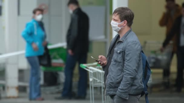 Ein maskierter Mann wartet mit einem Coronavirus. Menschen stehen mit mobilen Covid-19. — Stockvideo