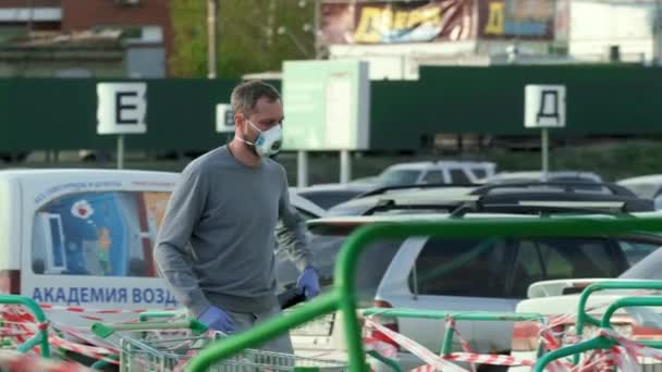 手袋のマスクの人は携帯電話のコロナウイルスを保持します。男歩く上の駐車｜covid-19. — ストック動画