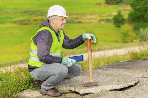 Operaio con sledgehammer e tablet PC vicino a lastre di cemento rotto — Foto Stock