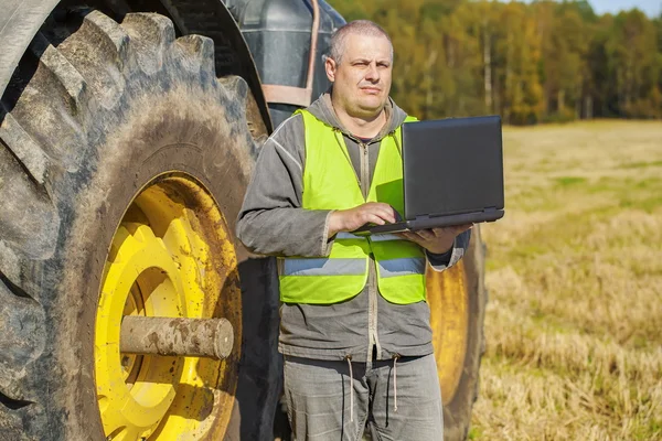 Agricultor con computadora cerca del tractor en el campo —  Fotos de Stock