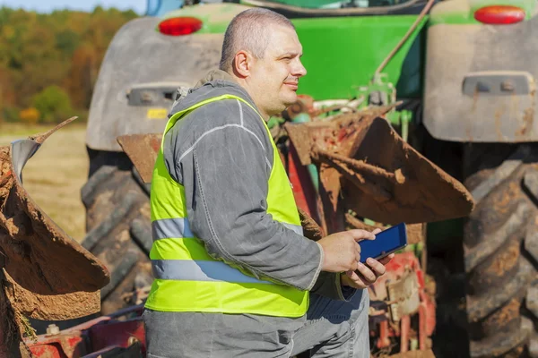 Agricultor con tablet PC cerca del tractor en el campo —  Fotos de Stock