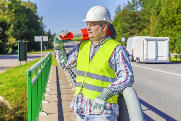 Road construction worker with traffic cone on shoulder near highway — Stock Photo, Image