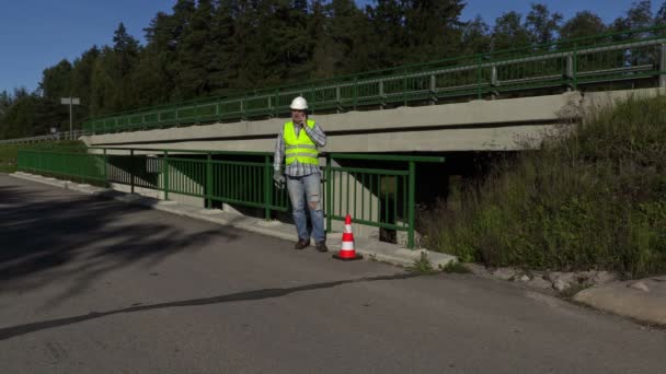 Road construction worker talking on phone on bridge near highway — Stock video