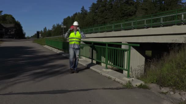 Trabajador de la construcción de carreteras hablando por teléfono en el puente cerca de la carretera — Vídeos de Stock