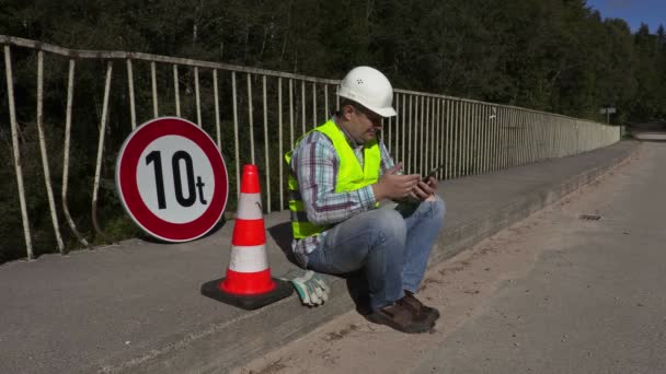 Lucrător în construcții rutiere așezat și folosind tabletă PC — Videoclip de stoc