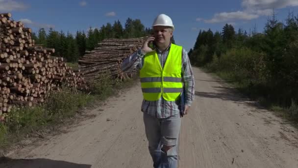 Holzfäller telefonieren mit Smartphone und laufen in der Nähe von Holzstapeln — Stockvideo