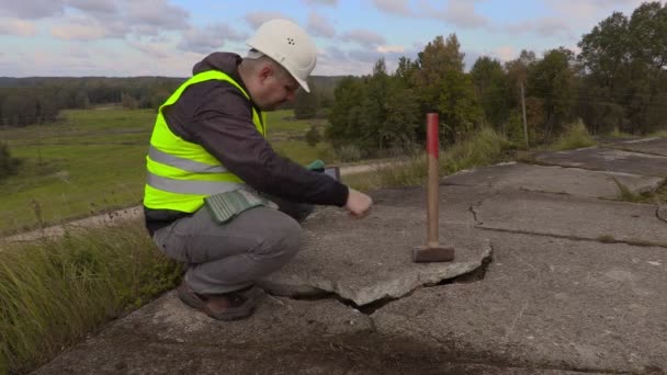 Работник с кувалдой с помощью планшетного ПК возле сломанных бетонных плит — стоковое видео